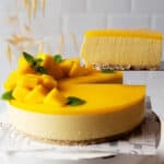 Taking a slice of healthy no bake mango cheesecake from a cake stand