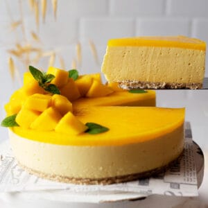 Taking a slice of healthy no bake mango cheesecake from a cake stand