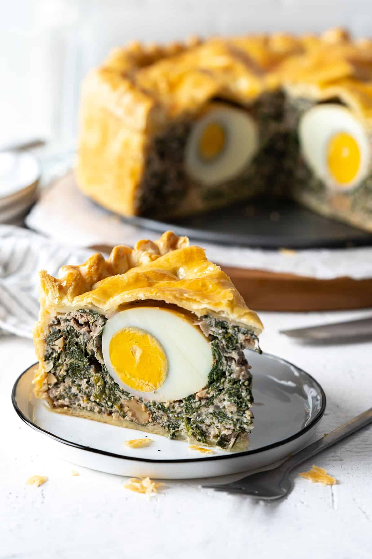 Una porción de pascualina (tarta de espinacas y ricotta) en un plato con la tarta entera al fondo.